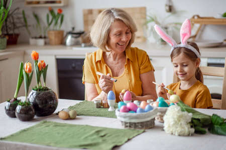 Happy easter family elderly grandmother and little granddaughter with rabbit ears are preparing for the holiday to paint eggsの写真素材