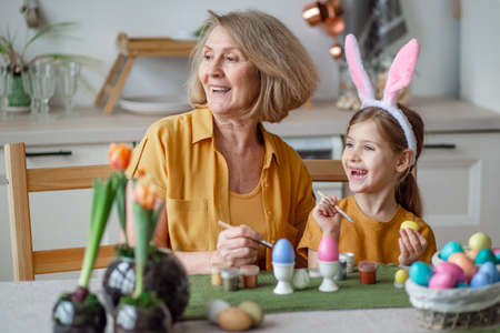 Happy easter family elderly grandmother and little granddaughter with rabbit ears are preparing for the holiday to paint eggsの写真素材