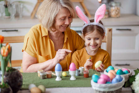 Happy easter family elderly grandmother and little granddaughter with rabbit ears are preparing for the holiday to paint eggsの写真素材