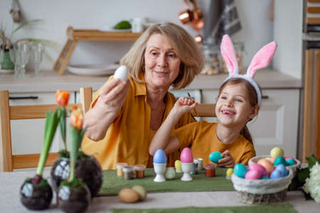 Happy easter family elderly grandmother and little granddaughter with rabbit ears are preparing for the holiday to paint eggsの写真素材