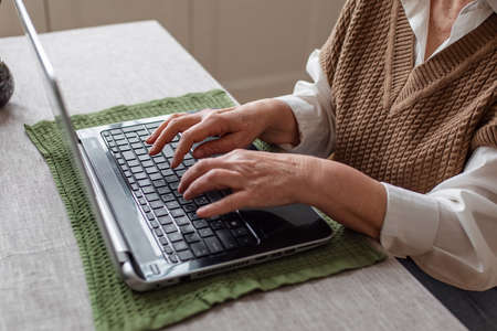 Close-up of an elderly womans hand on a laptop keyboard while working remotely at home typing the...