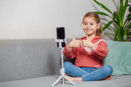 Small blonde blogger girl, an influential person, communicates with subscribers, conducts a live broadcast with a cat, looks at the smartphone screen at home. When taking a selfie, call your friends.の写真素材