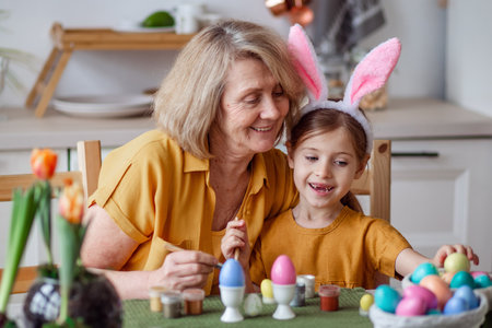 Happy easter family elderly grandmother and little granddaughter with rabbit ears are preparing for the holiday to paint eggsの写真素材