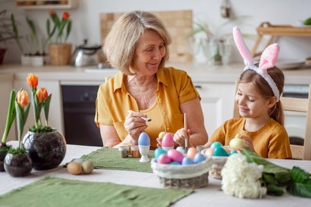 Happy easter family elderly grandmother and little granddaughter with rabbit ears are preparing for the holiday to paint eggsの写真素材