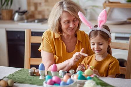 Happy easter family elderly grandmother and little granddaughter with rabbit ears are preparing for the holiday to paint eggsの写真素材