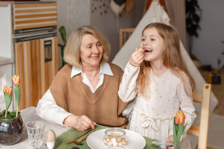 Elderly woman grandmother and little granddaughter joyfully set the table at home in the kitchen,...
