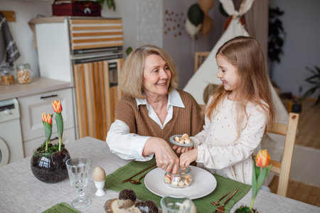 Elderly woman grandmother and little granddaughter joyfully set the table at home in the kitchen, learn etiquetteの写真素材