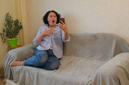 Girl talking on the phone online sitting on the couchの写真素材