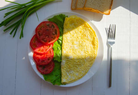 Scrambled eggs, an omelet of two eggs on a white plate with vegetables. Healthy breakfast on a light wooden backgroundの写真素材
