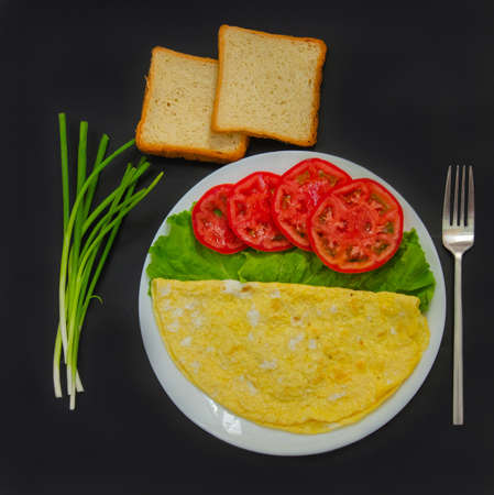 Scrambled eggs, an omelet of two eggs on a white plate with vegetables. Healthy breakfast on a dark backgroundの写真素材