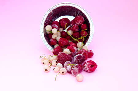 A set of frozen raspberries and currants of red and white color in a foil plate on a light backgroundの写真素材