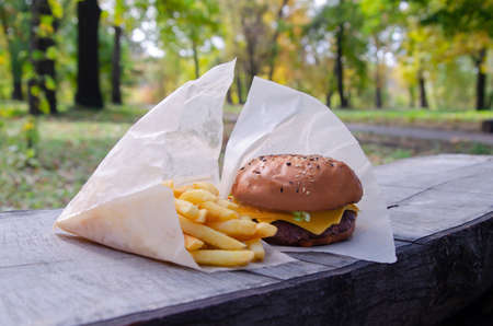 French fries and a burger in a paper bag on a wooden background. Eating in the park in natureの写真素材