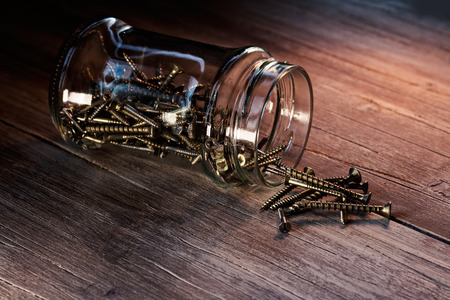 Jar filled with screws on a wooden tableの写真素材