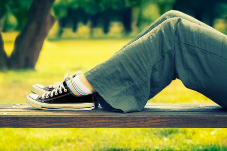 Woman's legs in a black canvas and green linen pants sneakers sitting on a bench.の写真素材