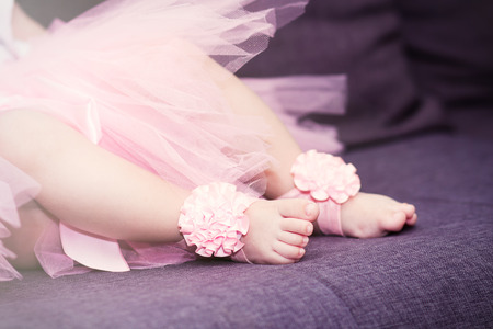 Little baby feet in ballet tutu dress and pink slippers sitting on the sofaの写真素材