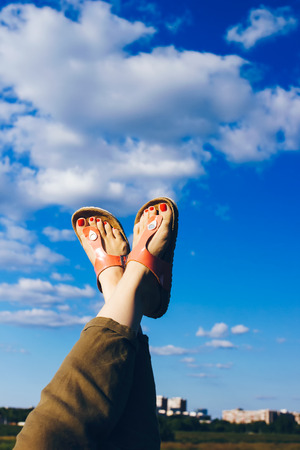 Woman's feet in orange sandals up in the air against blue sky and white cloudsの写真素材