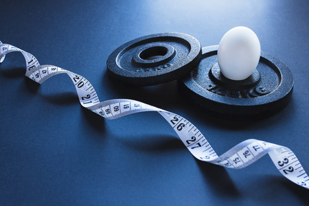 Steel weightlifting plates with tape measure and one white boiled eggの写真素材