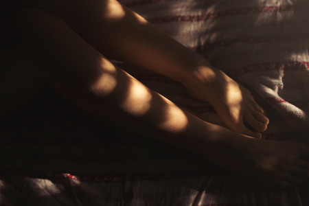 Woman's legs on bed sheets with sun rays coming thru the blindsの写真素材