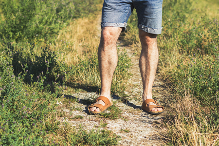 Male legs in brown leather sandals and blue jean shorts standing on a trailの写真素材