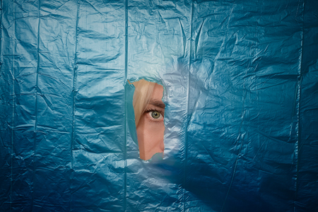 Woman's eye looking through torn off blue nylon barrierの写真素材