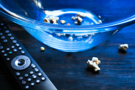 Almost empty bowl of popcorn and TV remote, illuminated with blue light from TV screen