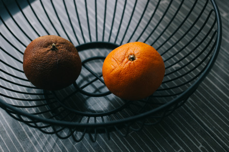 Two oranges in metal basket, one healthy and ripe, other brown and badの写真素材