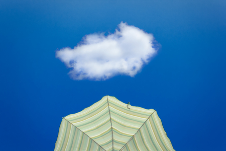 Yellow striped parasol against bright blue sky with one lonely white cloudの写真素材