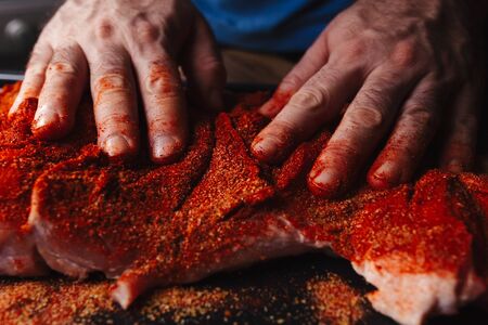 Man preparing raw piece of meat, rubbing different spices and herbs in it before roasting