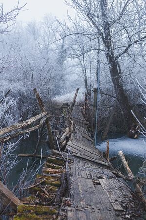 Old wooden weathered bridge over river, broken and collapsed