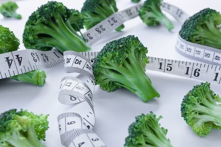 Broccoli florets on white background with white measuring tape intertwined between, diet concept