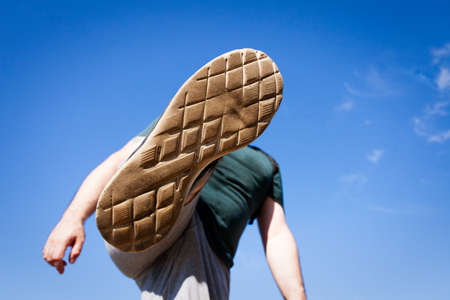 Man raising his foot high in the air in attempt to kick or stomp someone or something , view from under his footの写真素材