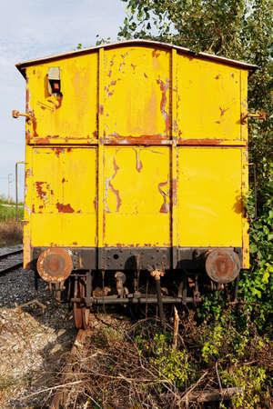 Back view of an old yellow train, abandoned and rusty, on an old tracks in the natureの写真素材