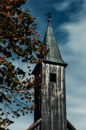 Black church bell tower, ominous in the background, autumn tree branch in front of itの写真素材