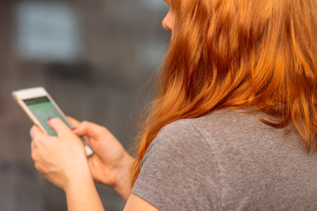 Woman with red hair scrolling on her phone, over the shoulder look, social media conceptの写真素材