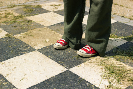 Woman in red sneakers and green pants standing outside on big black and white checkered squares filled with cut grass and hayの写真素材