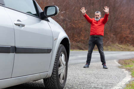 Man in red jacket on mountain road gesturing to car to stop, dangerous road ahead