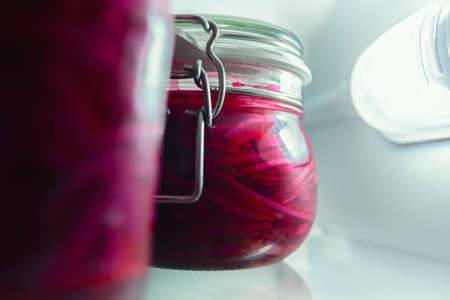 Pickled red onions in glass jars on a fridge shelf