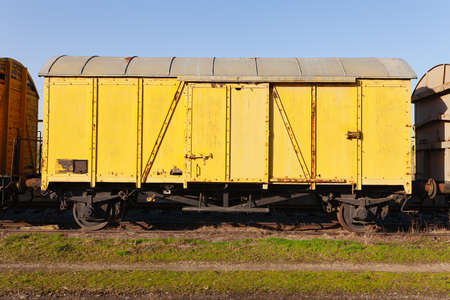 Old yellow cargo train wagon, grungy and weathered on the abandoned train tracks in fieldの写真素材