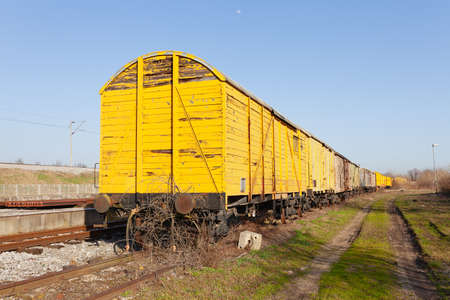 Abandoned yellow train wagon, weathered and rusty, on an old train tracksの写真素材