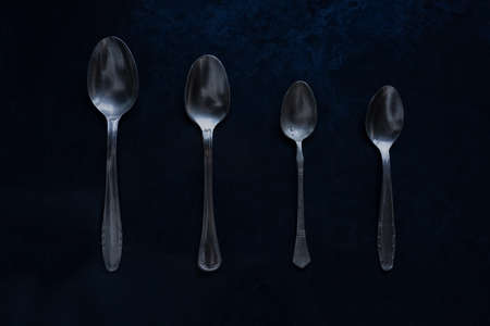 Retro looking 4 silver metal teaspoons on a dark, grungy backgroundの写真素材