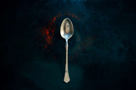 Vintage old teaspoon laying on dark background surrounded with red ground pepper spice, dark and spooky reflection in itの写真素材
