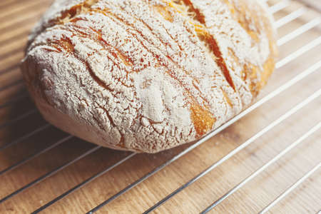 Freshly baked loaf of sourdough bread cooling on a cooling rack on a kitchen tableの写真素材