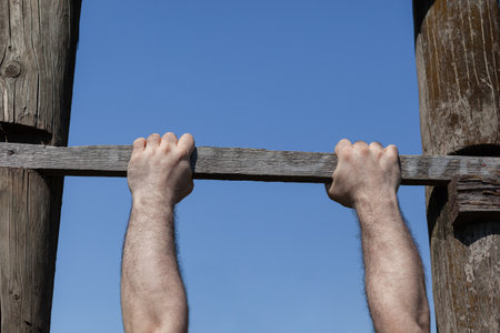 Strong male hands firm gripping wooden ladder step, hanging, blue sky in background