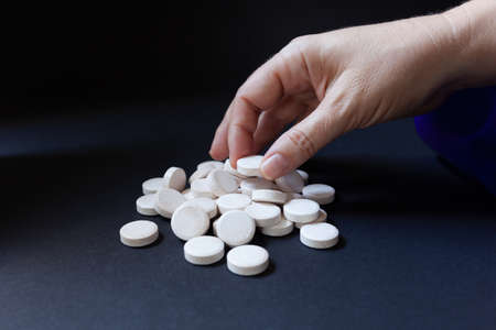 Woman's hand picking up one of the many white pill from dark backgroundの写真素材
