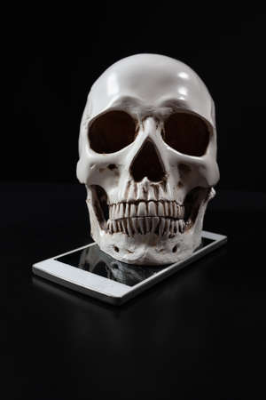 Human skull on top of smartphone with cracked screen on dark backgroundの写真素材