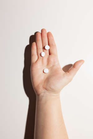 Three white pills on outstretched male palm on white backgroundの写真素材