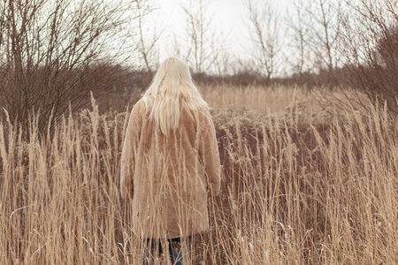 Anonymous woman with long blonde hair standing in the field, back viewの写真素材