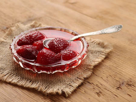 Homemade strawberry jam in glass bowl with spoon on wooden background