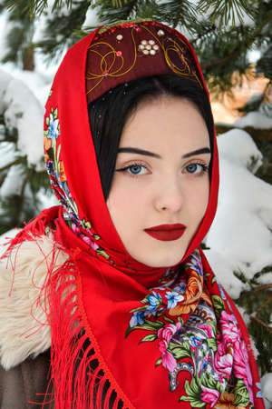 Beautiful Russian girl in a red shawl on the background of the winter forestの写真素材