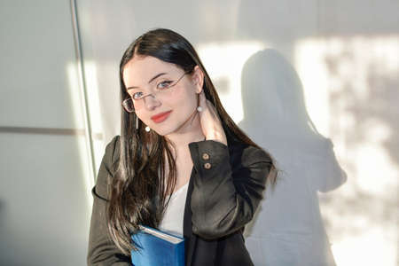 The girl with glasses squints from the sun. He holds a notebook in his hand, touches his neck with...